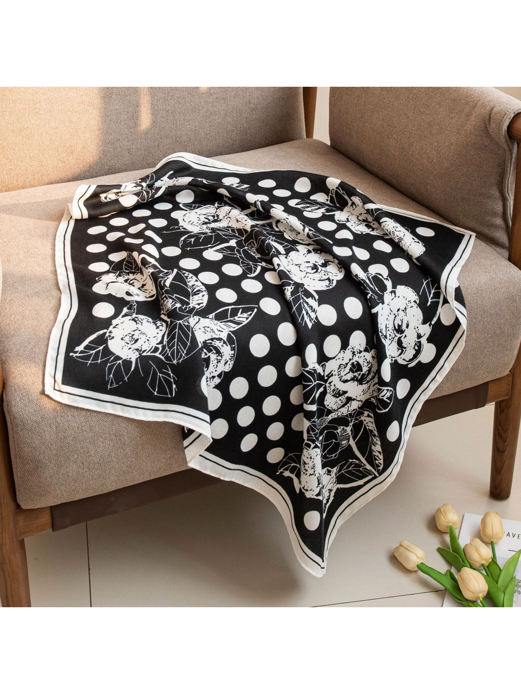 Black square scarf with white polka dots and floral motifs draped across an armchair