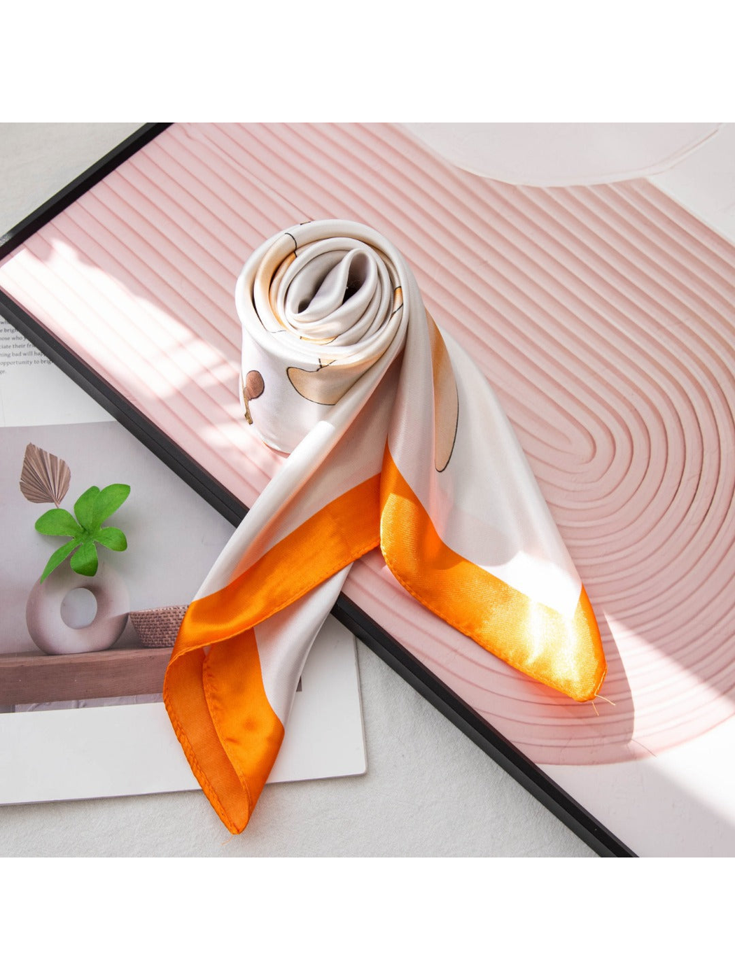 Rolled floral scarf with orange border displayed on a decorative book