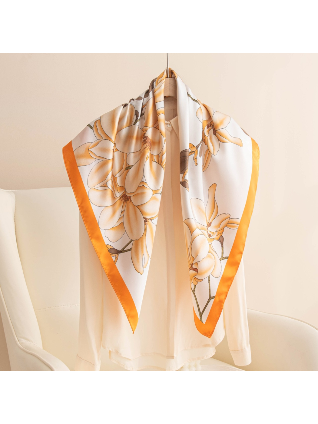 Orange-bordered floral square scarf draped over a cream blouse on a hanger