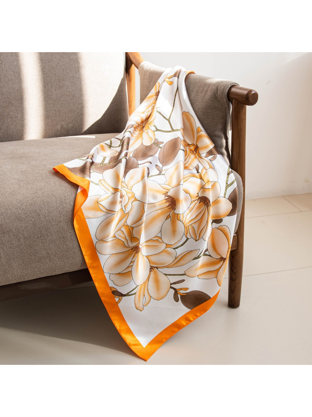 Orange-bordered floral square scarf draped over a gray armchair in sunlight