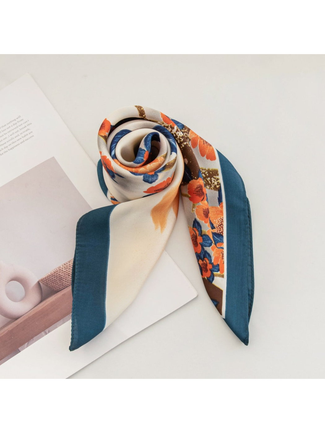 Cream floral square scarf rolled into a rosette with its teal border visible