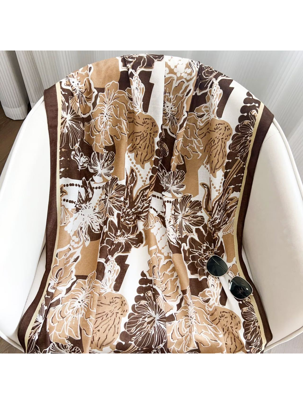 Brown floral scarf draped across a white chair with sunglasses