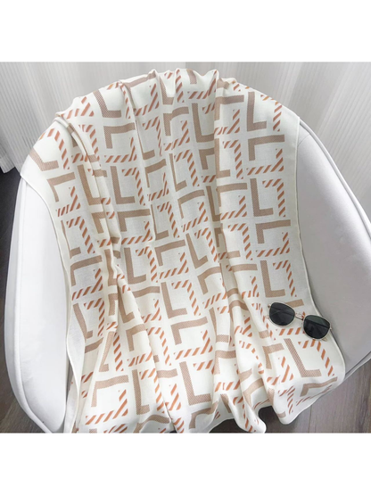 Ivory geometric scarf draped across a white chair with sunglasses