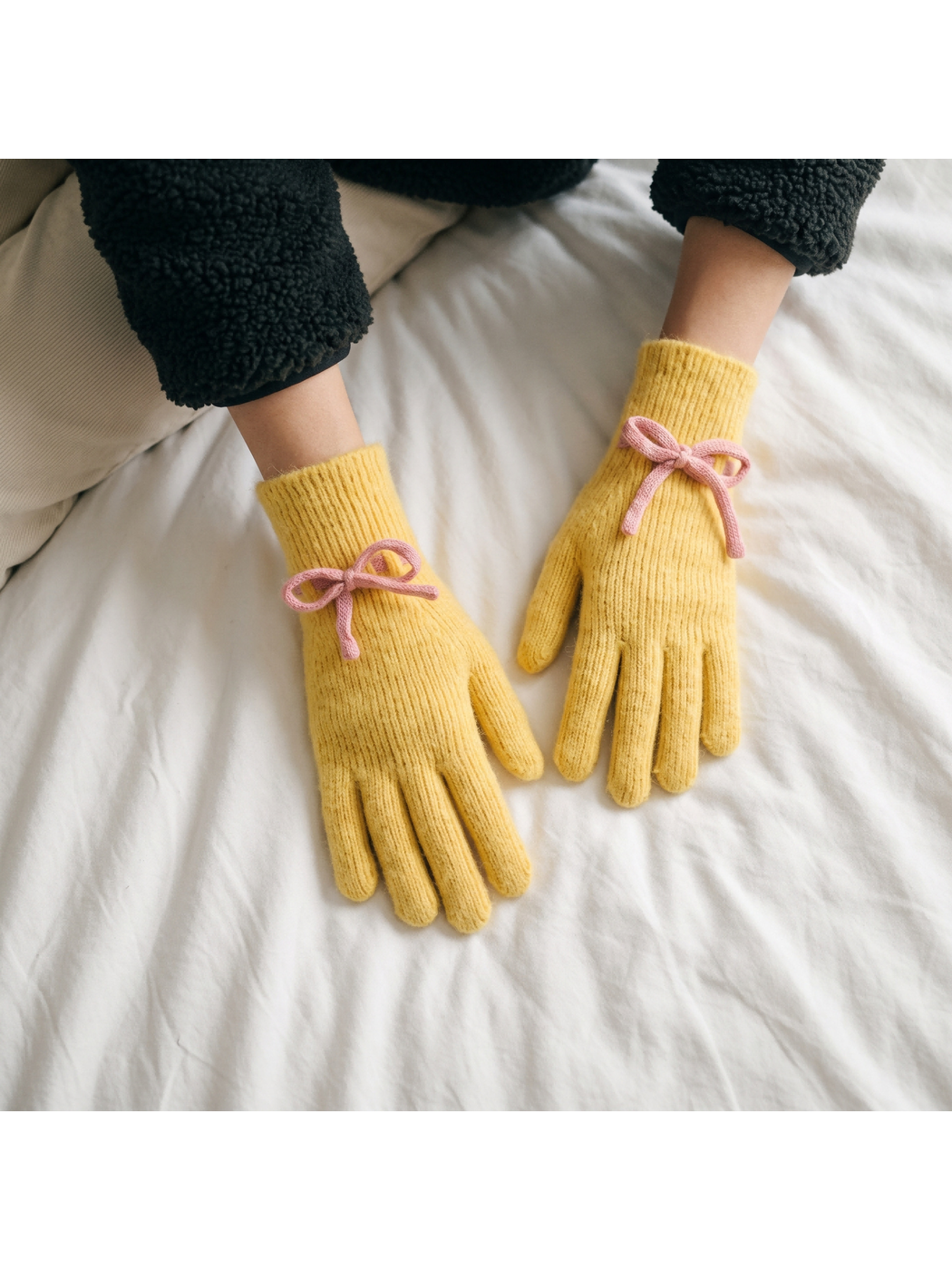 Yellow bow-detail gloves worn against white bedding