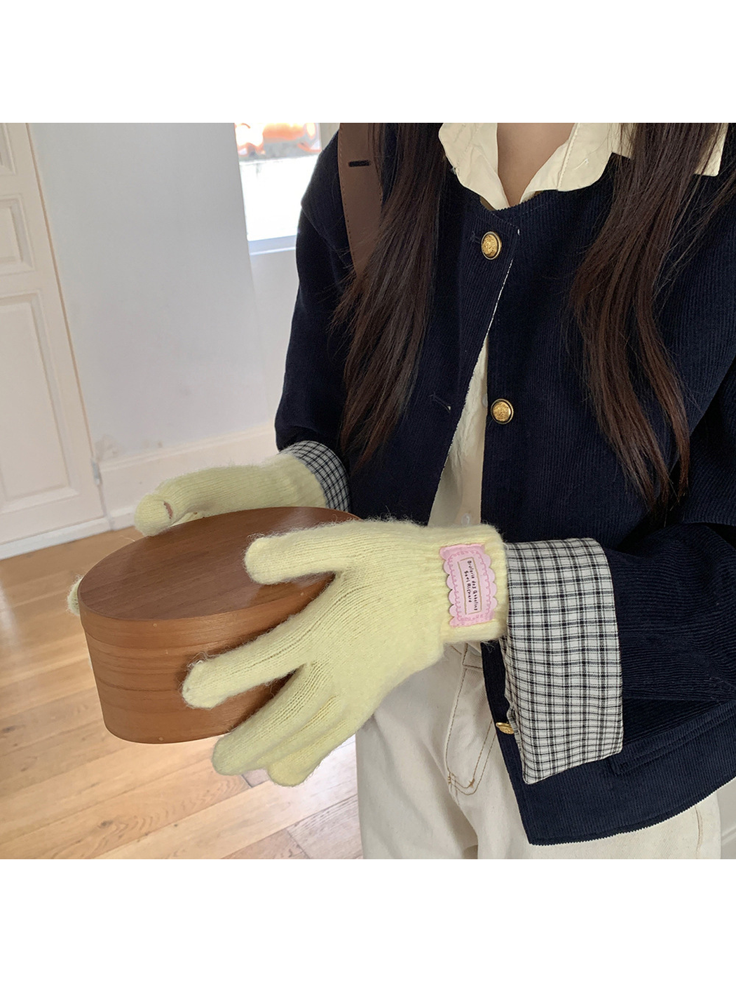 Yellow fuzzy knit gloves worn while holding a round wooden box