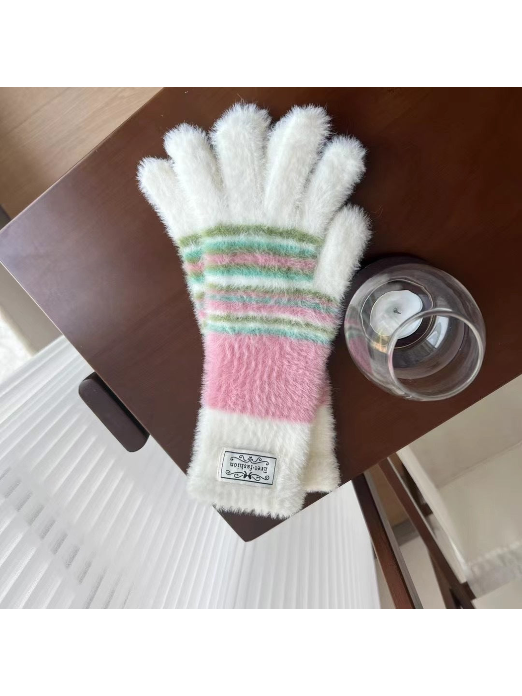 White fuzzy gloves with pink and green stripes, tabletop view