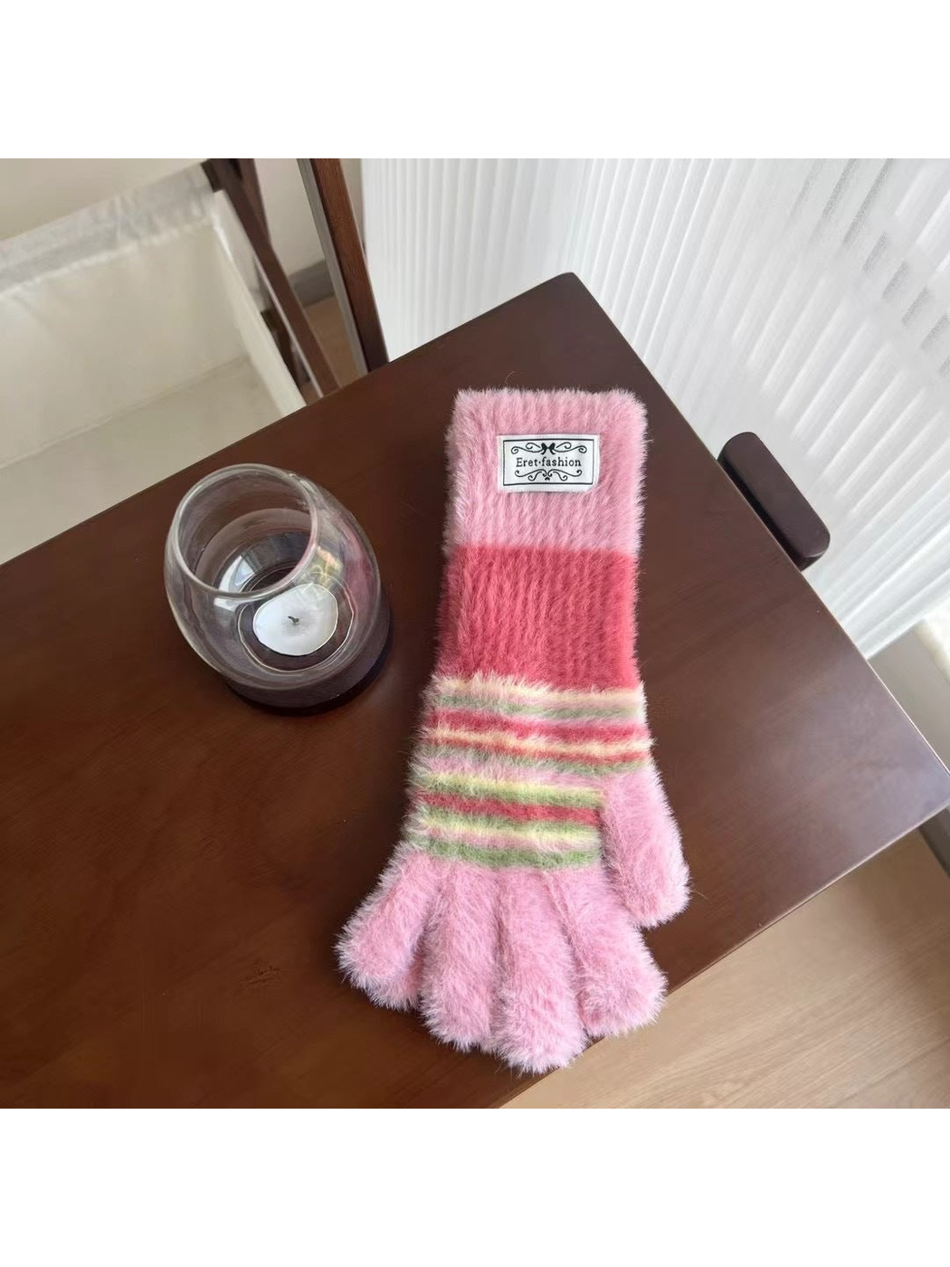 Pink fuzzy gloves with green and cream stripes, tabletop view