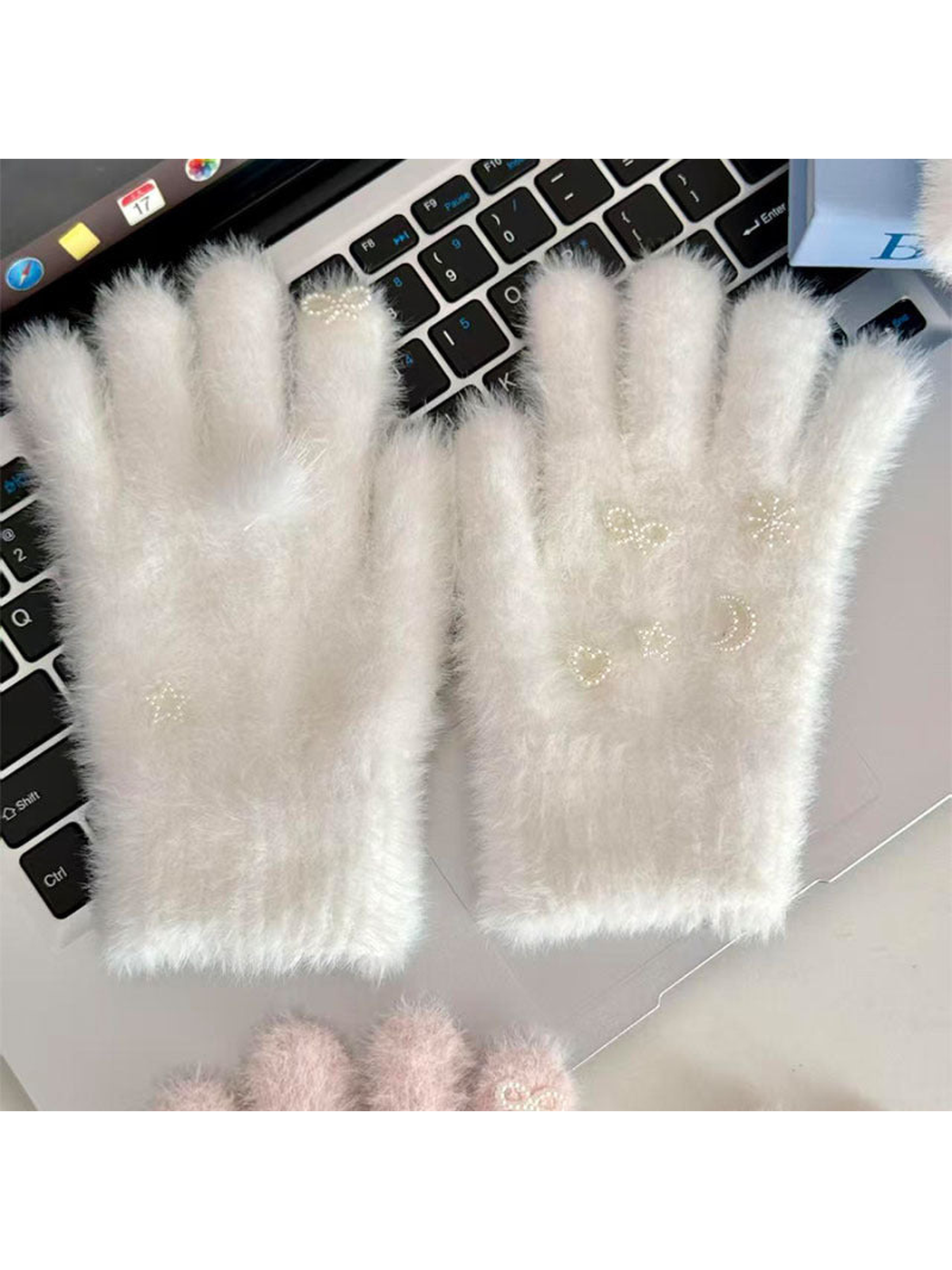 White fuzzy gloves with pearl-like celestial motifs displayed on a laptop