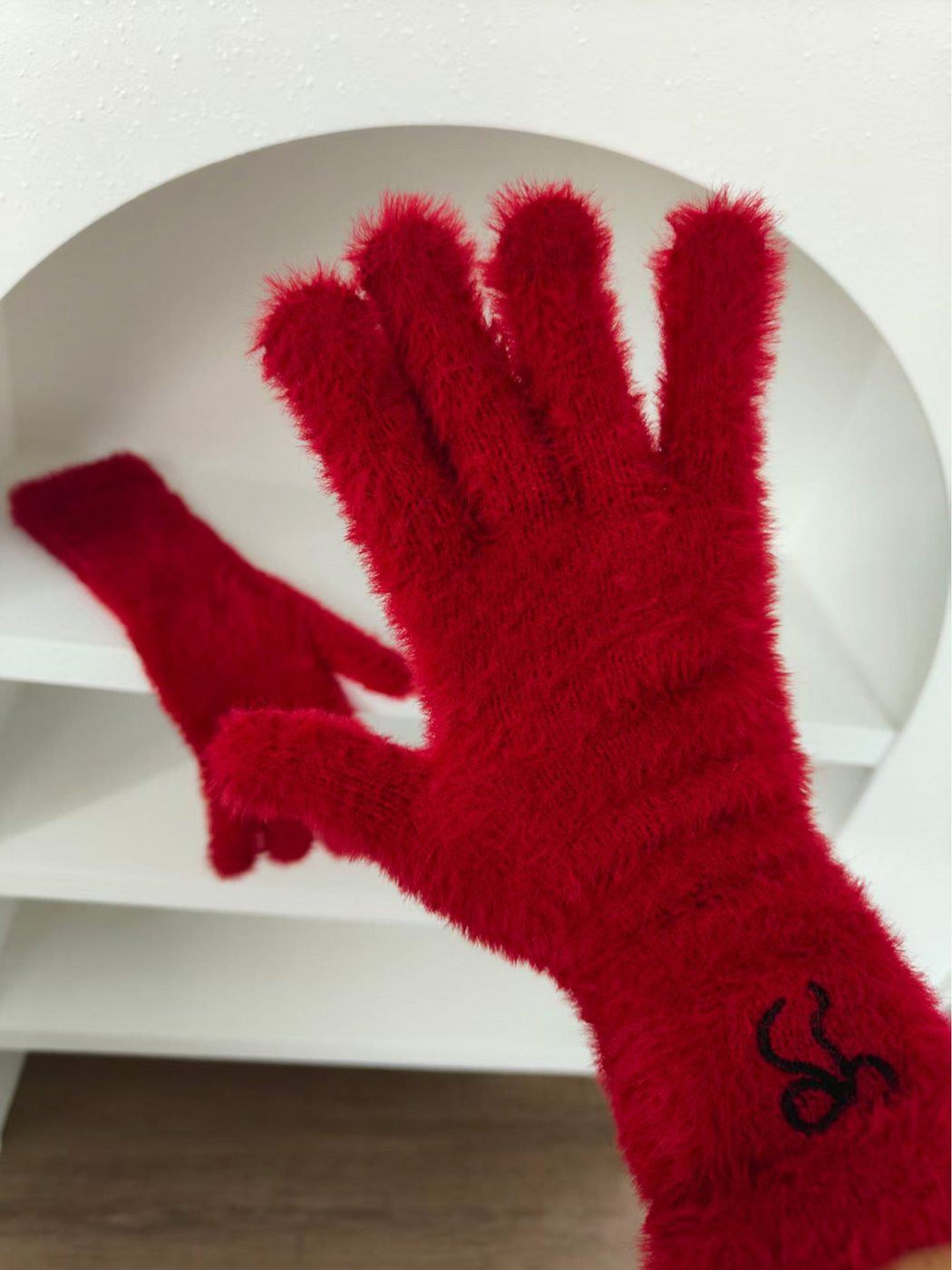 Red fuzzy glove worn on a hand with embroidered cuff motif