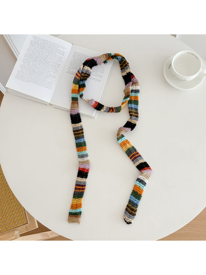 Multicolor striped narrow scarf arranged beside an open book and cup