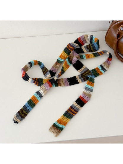 Multicolor striped narrow scarf spread across a table beside a brown bag