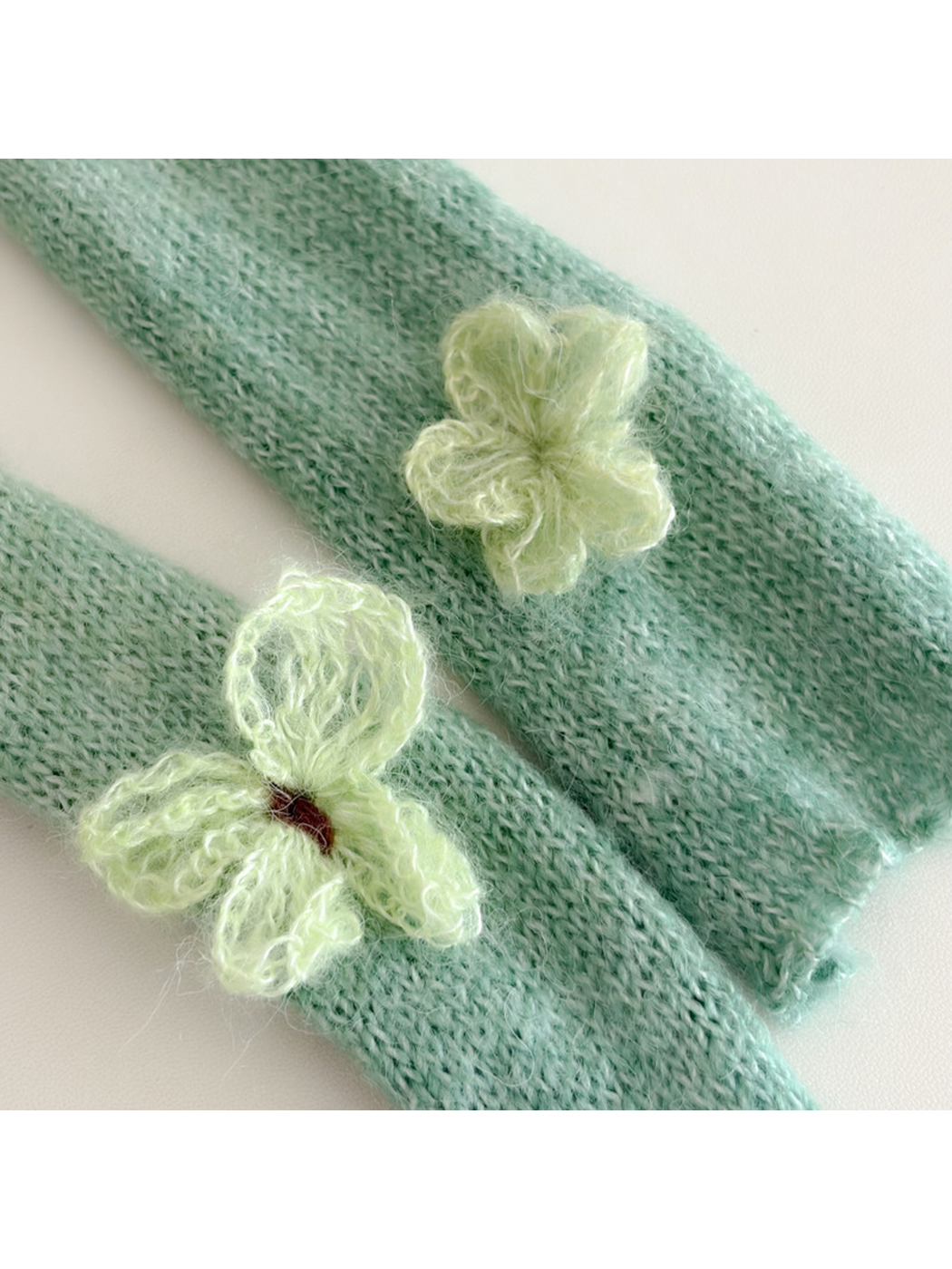 Close-up of raised butterfly appliqués on green knit scarf ends