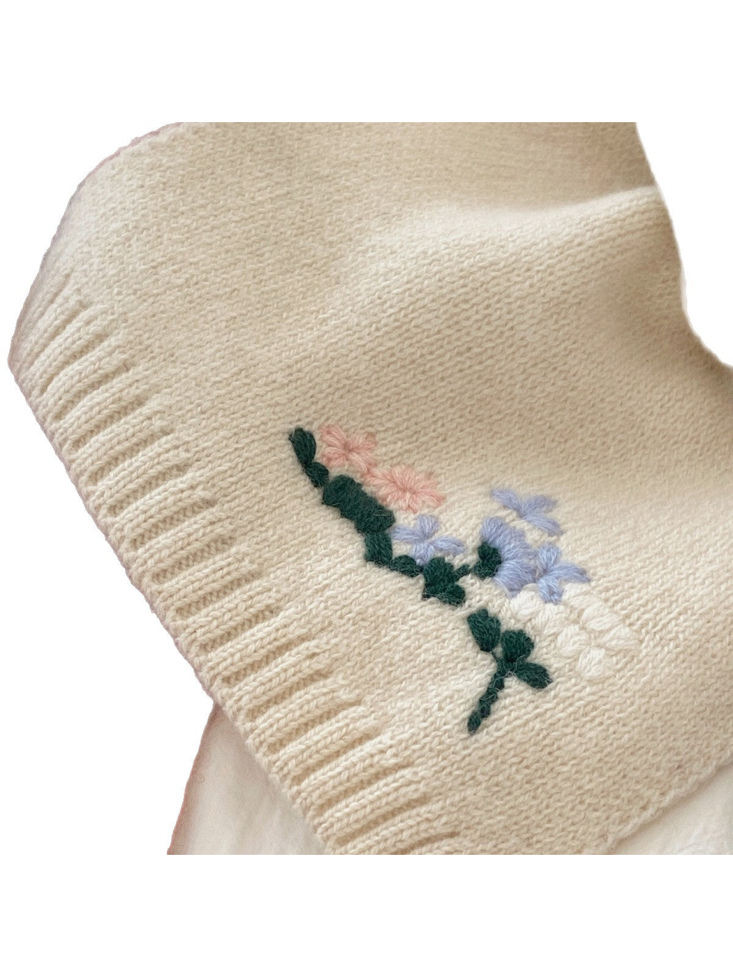 Close-up of the ivory scarf's floral threadwork and ribbed end