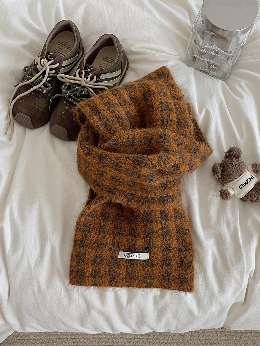 Orange checkered scarf arranged on white bedding with casual accessories