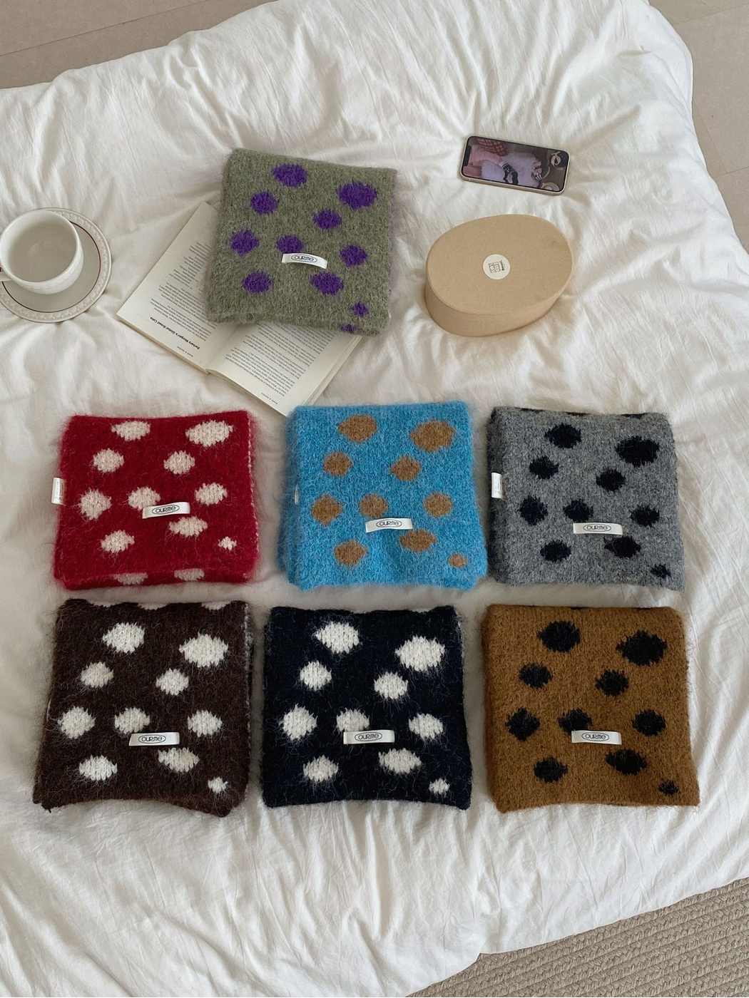 Seven irregular polka dot scarf styles arranged on a white bedspread