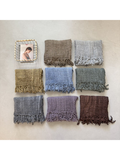 Eight color variations of the openwork fringed scarf arranged in a flat lay