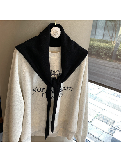 Black triangle scarf tied over a cream sweatshirt