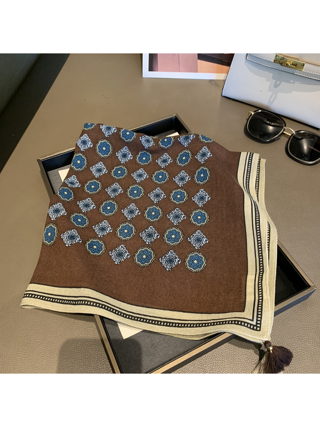 Folded brown square scarf showing blue floral medallions, cream border and corner tassels