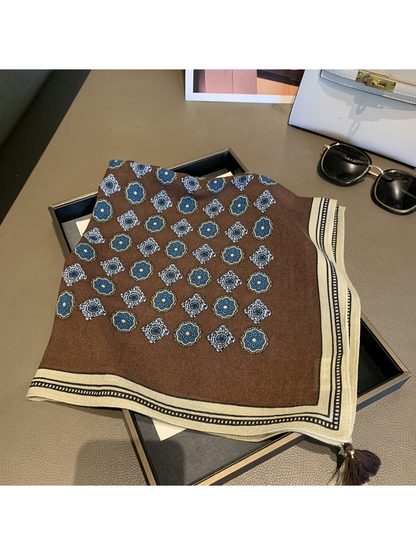 Folded brown square scarf showing blue floral medallions, cream border and corner tassels