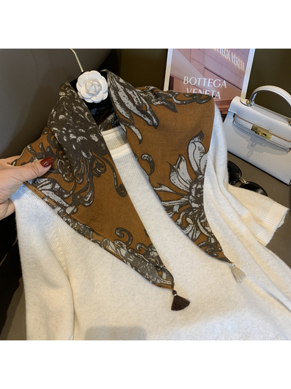 Warm brown floral scarf styled over a white sweater with tassels visible