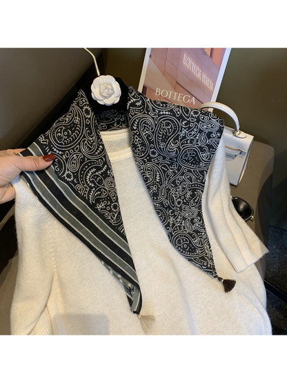 Black paisley scarf draped over a white sweater to show the striped border and tassels