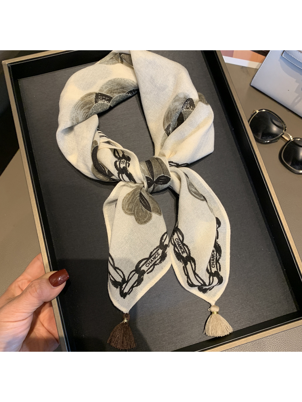Ivory floral scarf tied in a bow with chain-style border and contrasting tassels