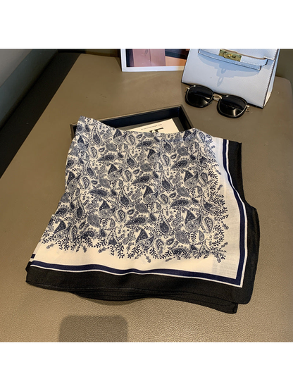 Navy and cream paisley square scarf laid flat with striped black border