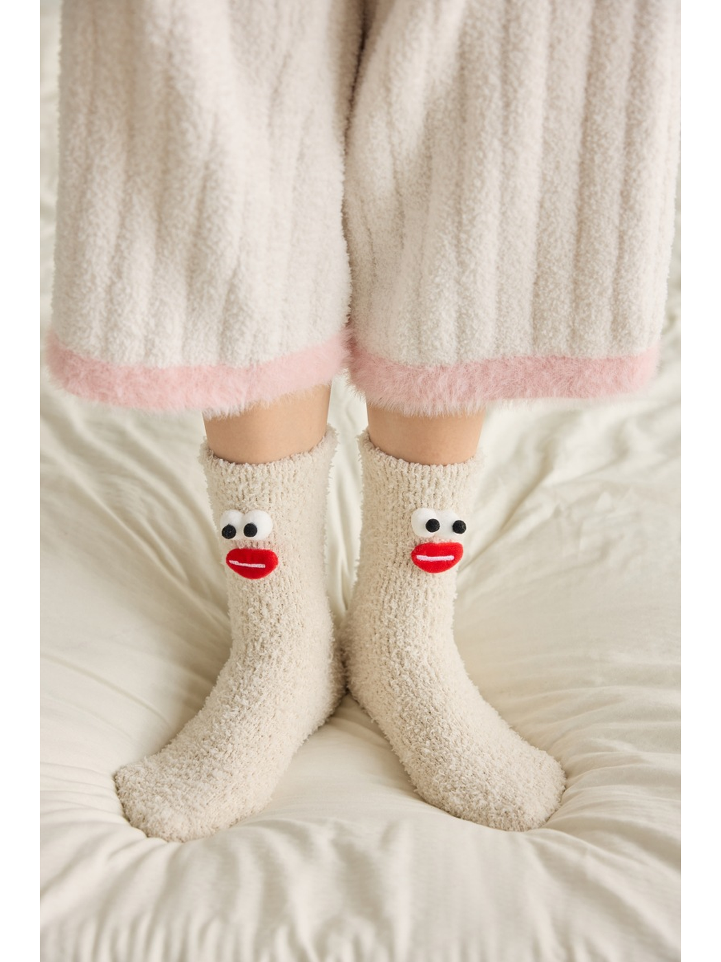 Beige fuzzy cartoon face crew socks worn on a bed