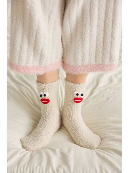 Beige fuzzy cartoon face crew socks worn on a bed