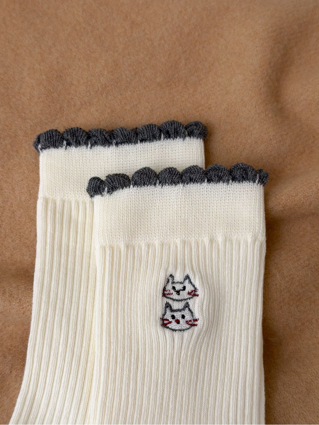 Close-up of Ivory sock scalloped cuff and stacked cat embroidery