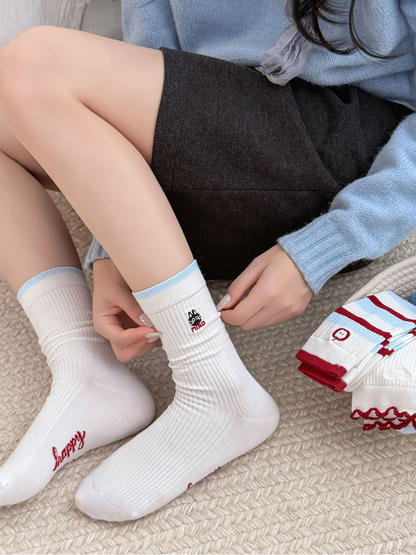Cat style white crew socks worn while seated beside folded striped and textured styles