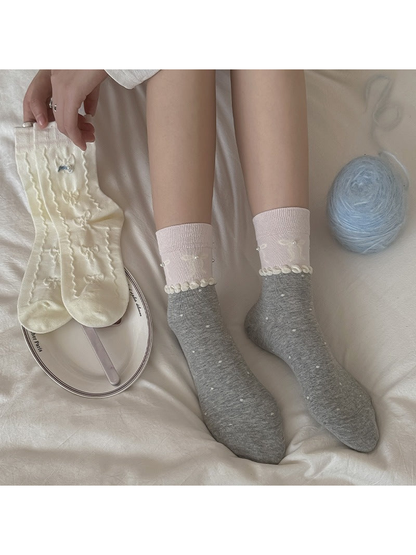 Gray polka-dot crew socks worn with pink cuffs beside ivory bow-pattern socks