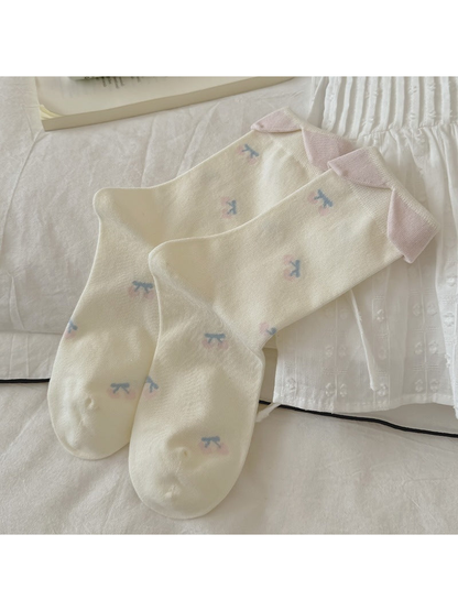 Ivory crew socks with scattered cherry motifs and pink folded cuffs, laid flat
