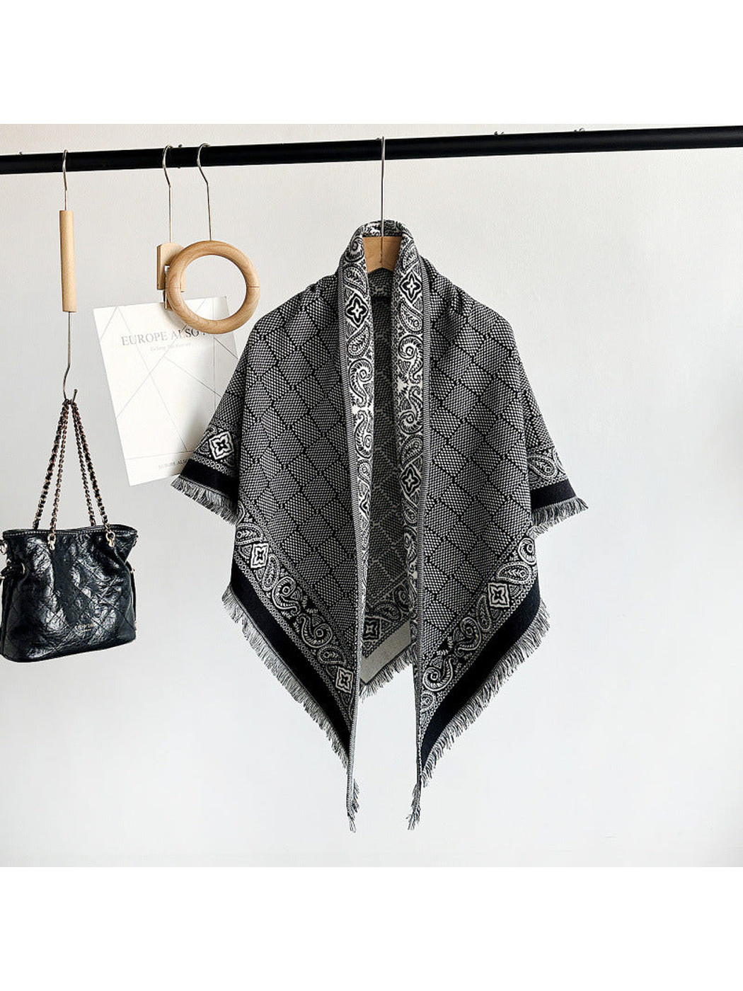 Black geometric scarf with paisley border and short fringe displayed on a hanger