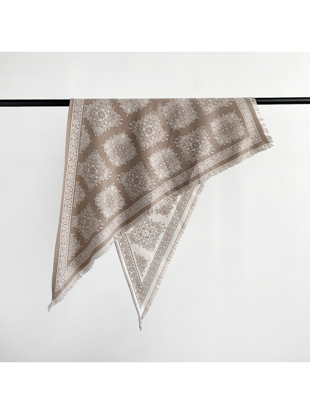 Khaki triangle scarf folded over a rail to show its medallion pattern, reverse side, and fringed edges