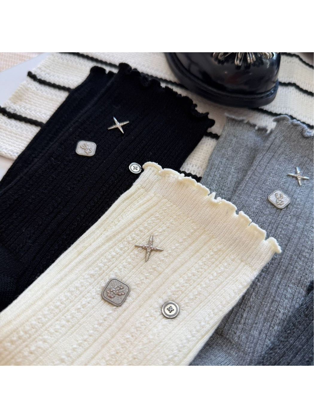 Close-up of black, ivory and gray socks with ribbed textures, ruffled cuffs and silver-tone accents