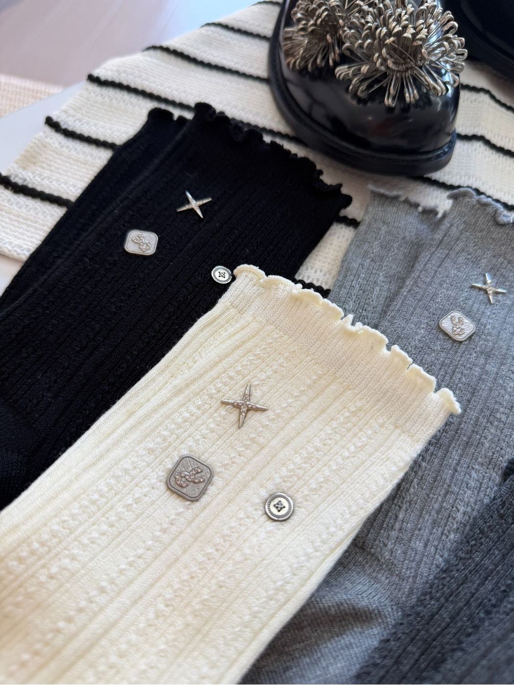 Close-up of black, ivory and gray socks with pointelle ribbing, ruffled cuffs and silver-tone motifs