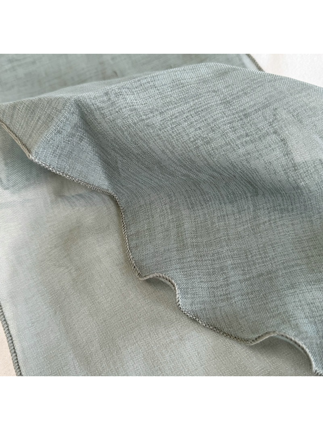 Close-up of the fine woven-look texture and wavy stitched scarf edge