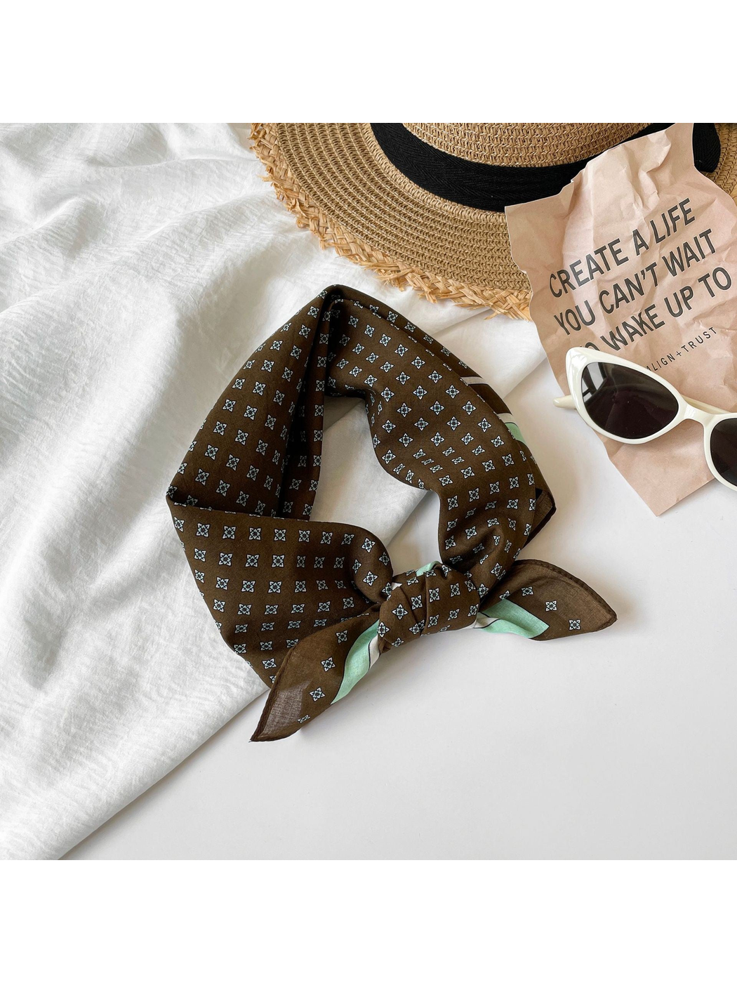 Brown geometric square scarf tied beside a wide-brim hat and sunglasses