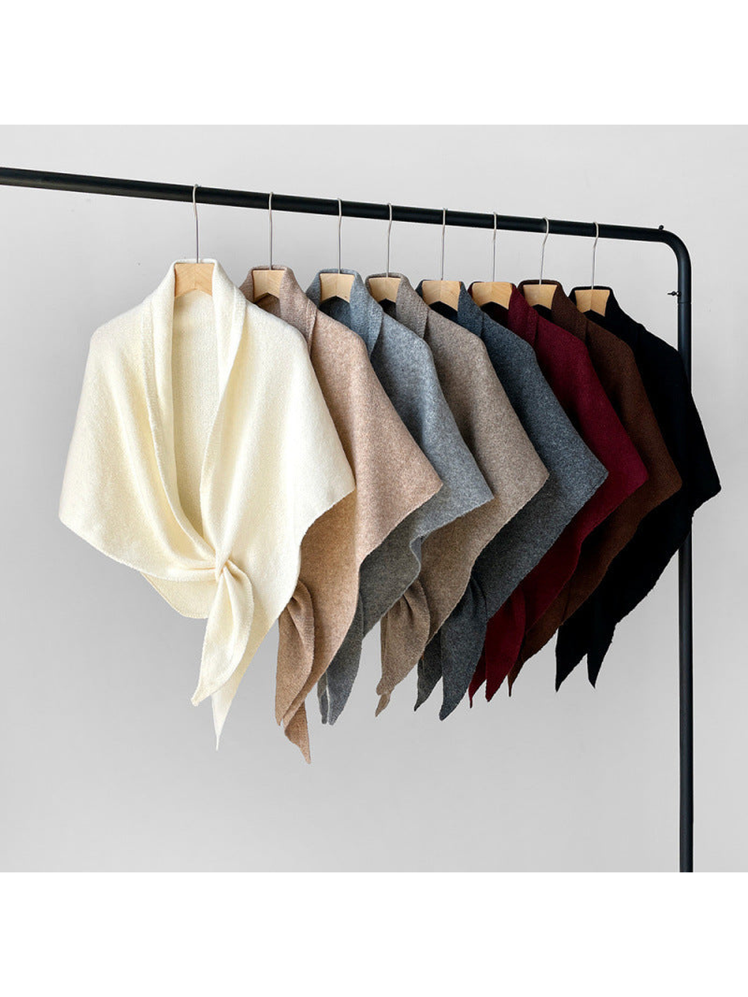 Multiple solid-color triangle shawls displayed on a garment rack