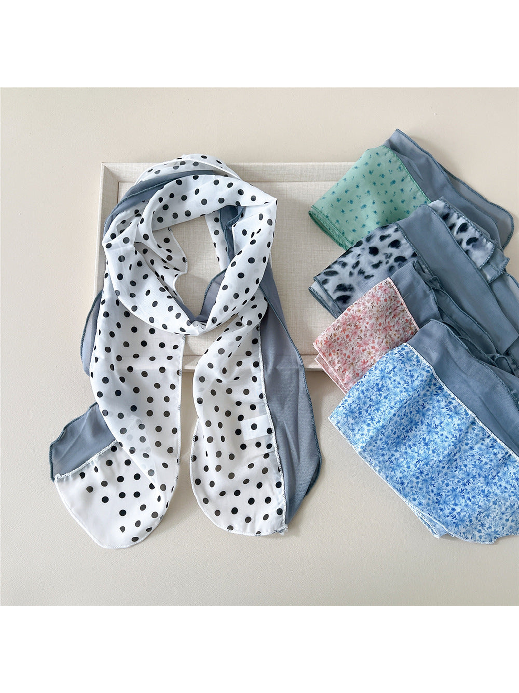 White dot scarf draped beside an assortment of floral and animal-print styles