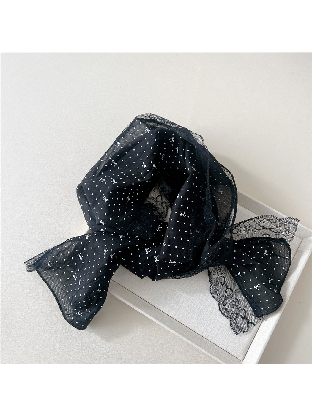 Black dotted bow scarf loosely draped over a neutral display tray