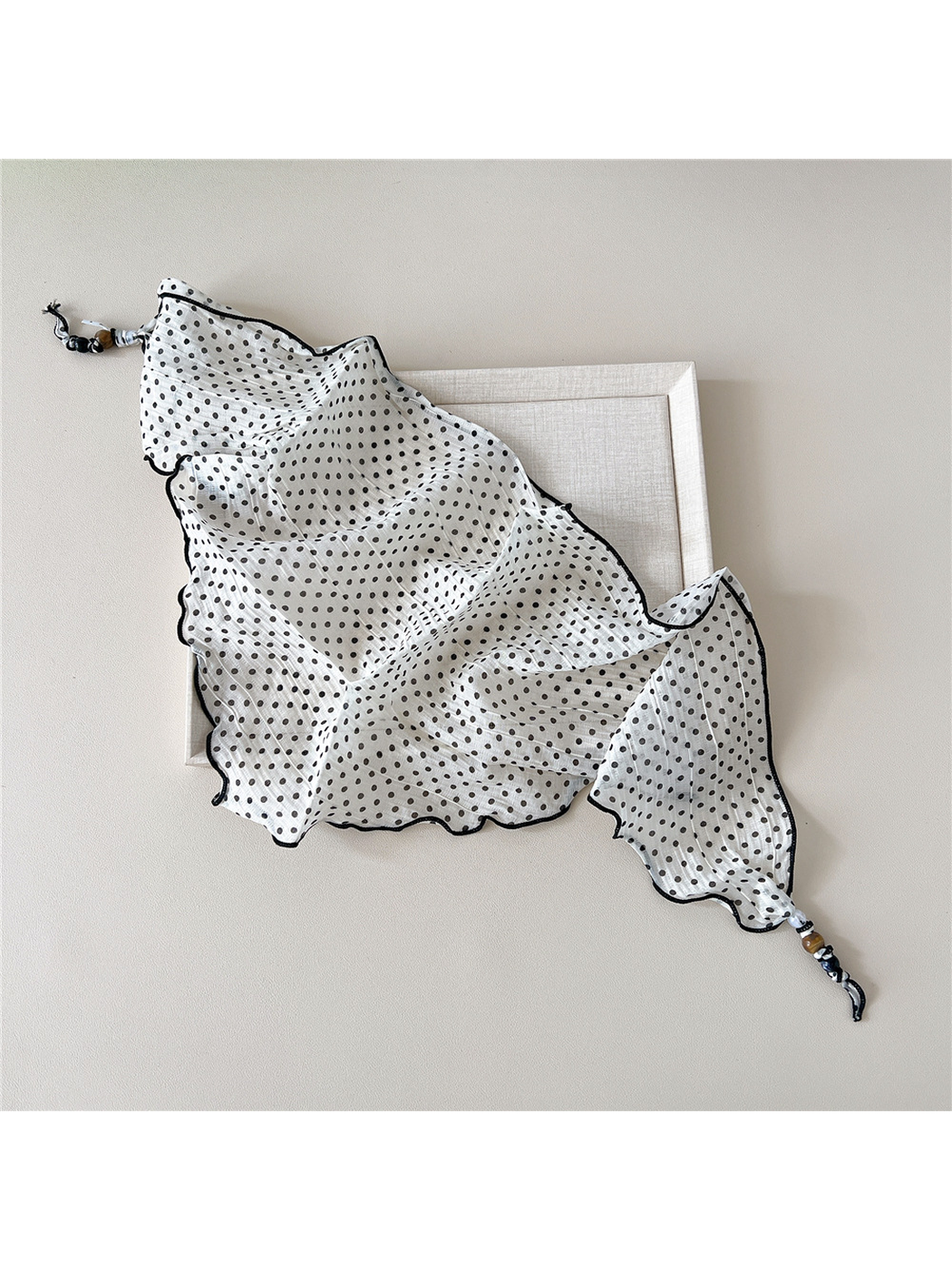 Ivory polka-dot triangular scarf spread open to show its wavy edges and beaded tips