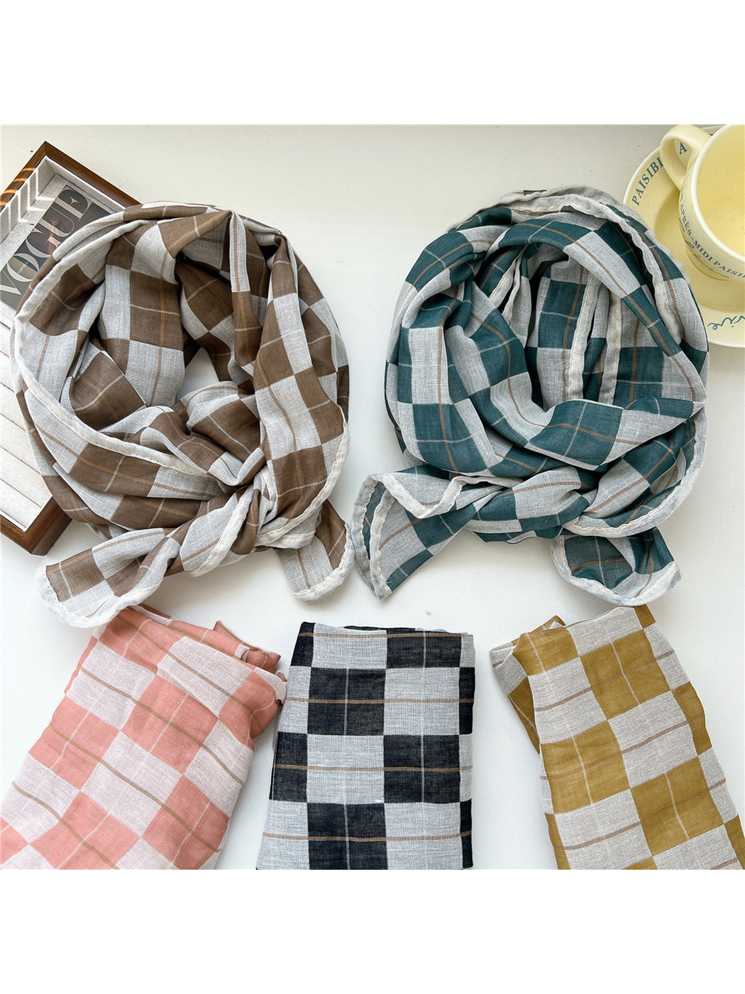 Brown and turquoise plaid scarves arranged above folded pink, black and yellow color options