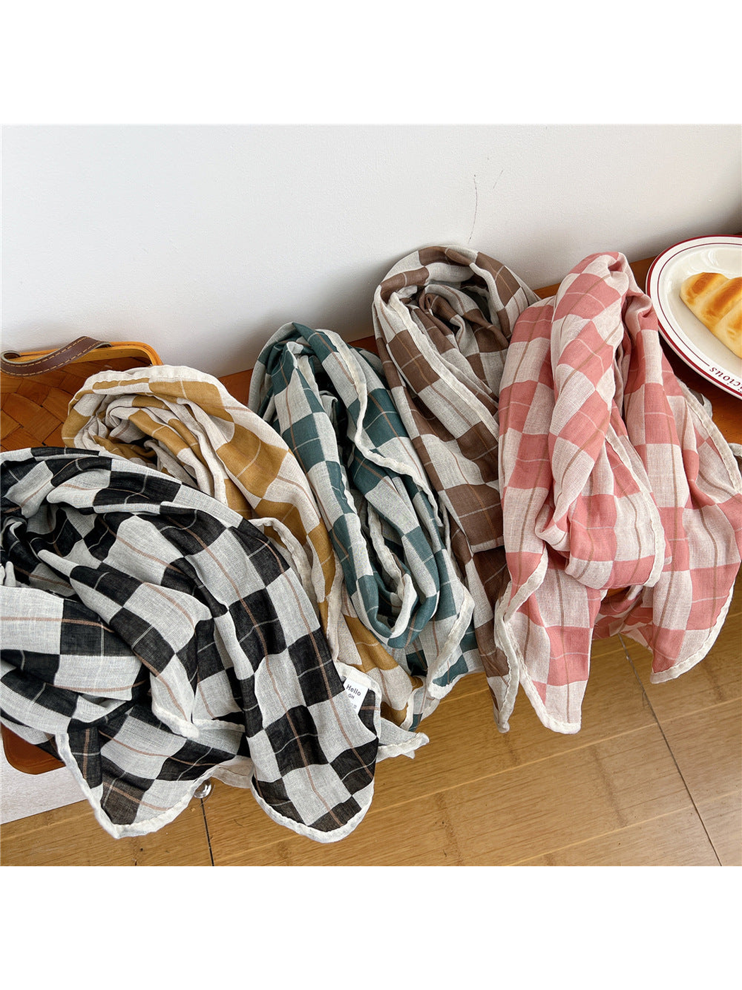 Five plaid scarf colors draped together on a wooden bench