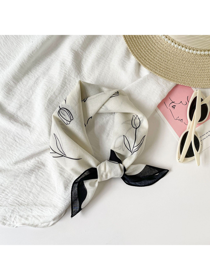 Black floral square scarf tied on a light tabletop
