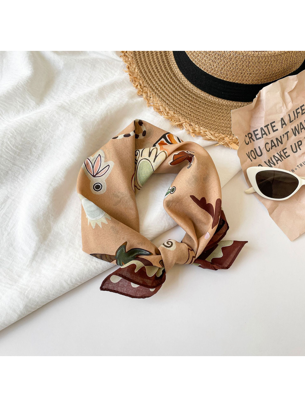 Brown patterned square scarf tied in a loose knot beside a sun hat