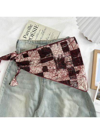 Red abstract mesh scarf spread across light-wash jeans