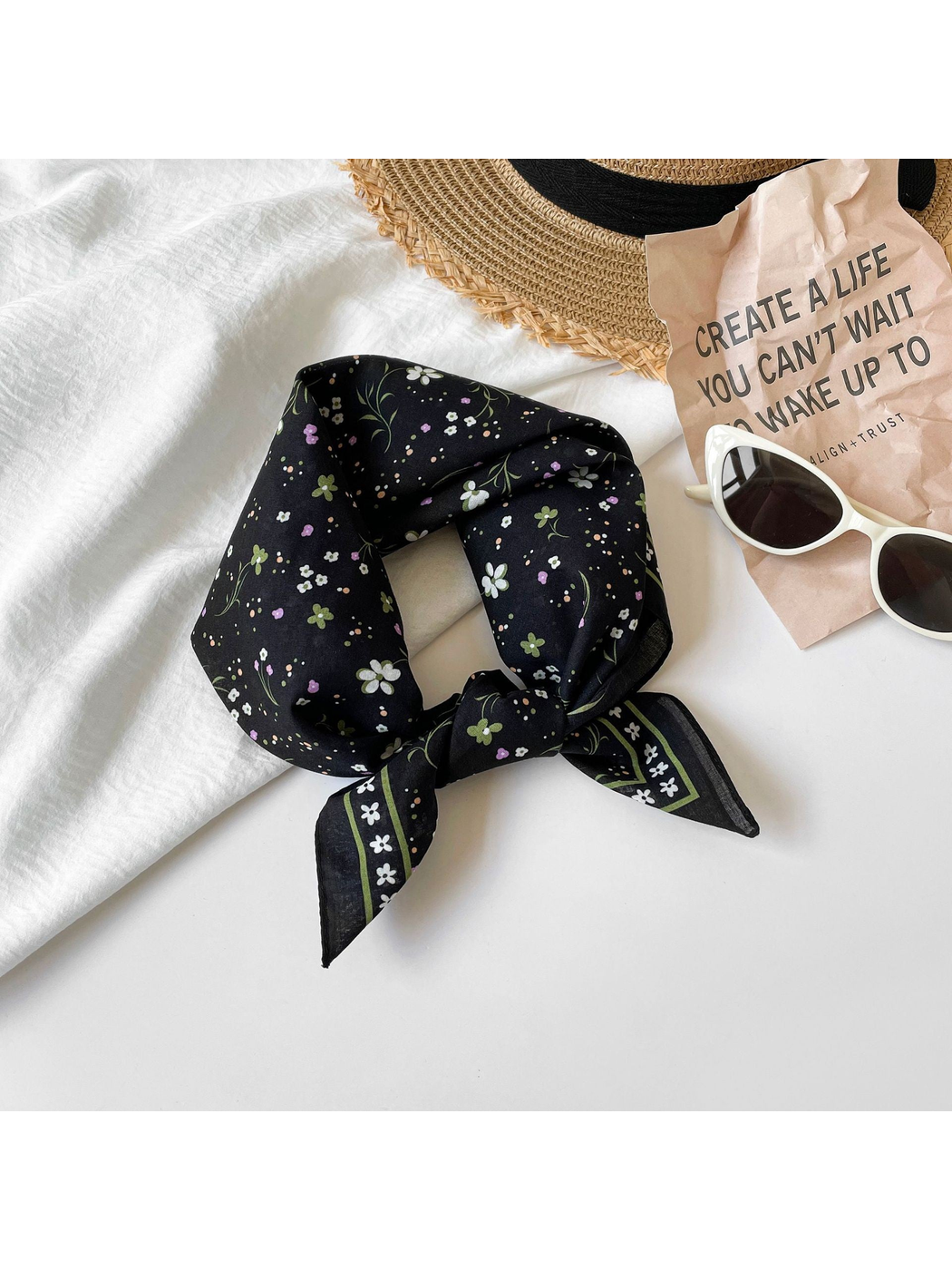 Black floral square scarf tied beside sunglasses and a sun hat