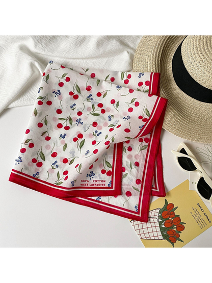 Cherry print square scarf folded beside a sun hat and sunglasses